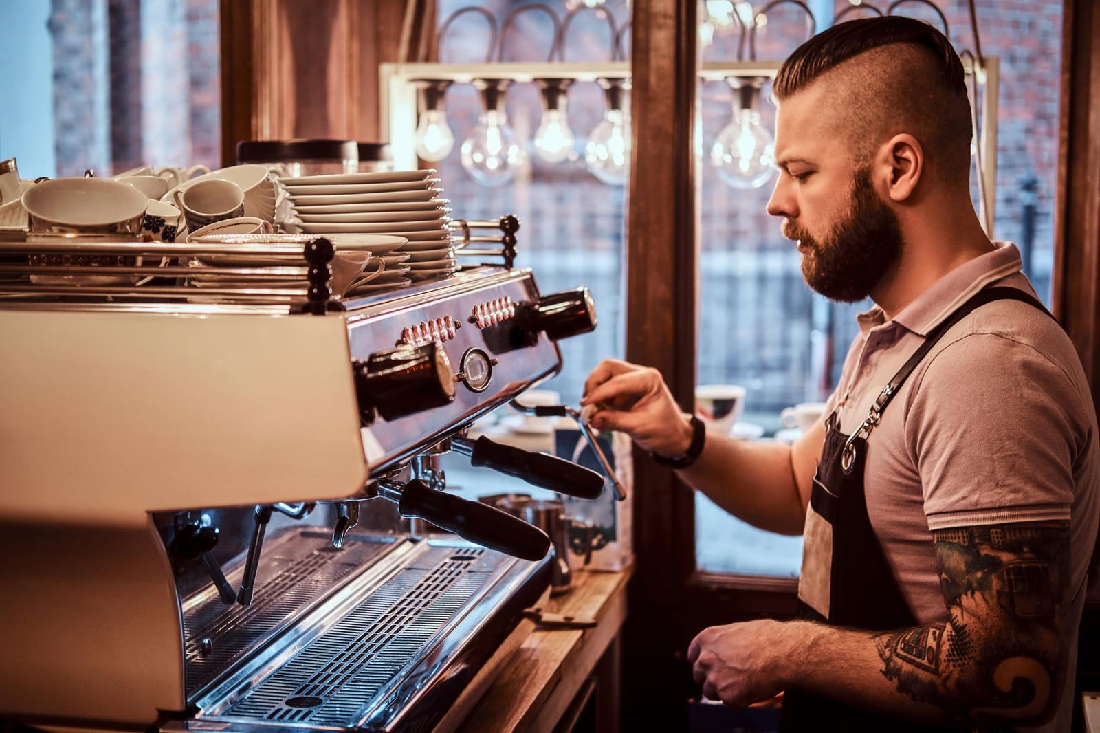 Barista uniformizado preparando café para um cliente no balcão
